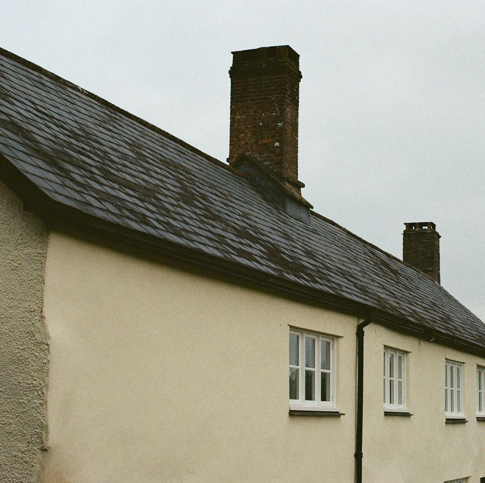 Cream cottage with a dark slate roof and a brick chimney stack at the gable