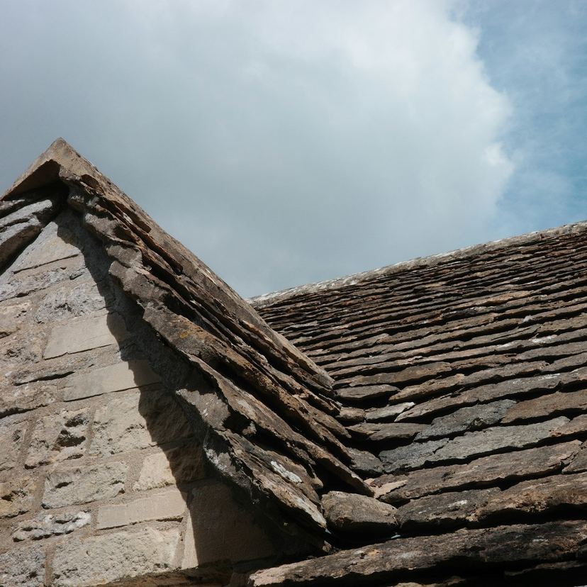 Old stone-slate roof slopes and a gable end under a cloudy sky